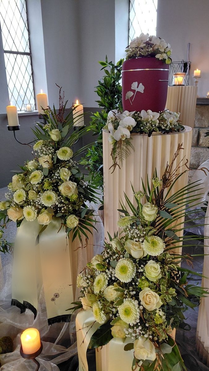 Urne mit Blumenschmuck und Trauergestecken in einer Kirche